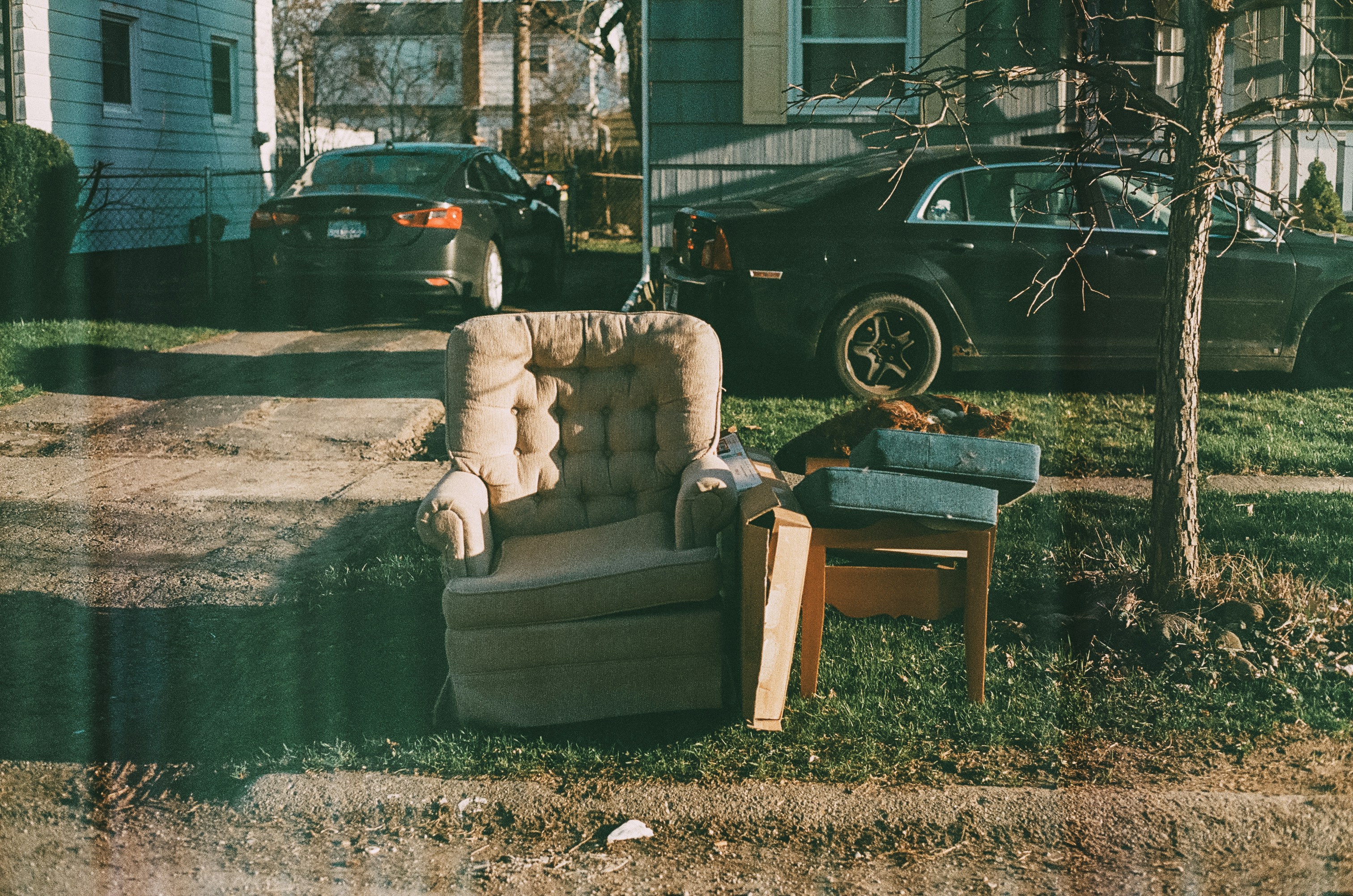 Old armchair and discarded furniture left on a lawn by a driveway in a residential neighbourhood.