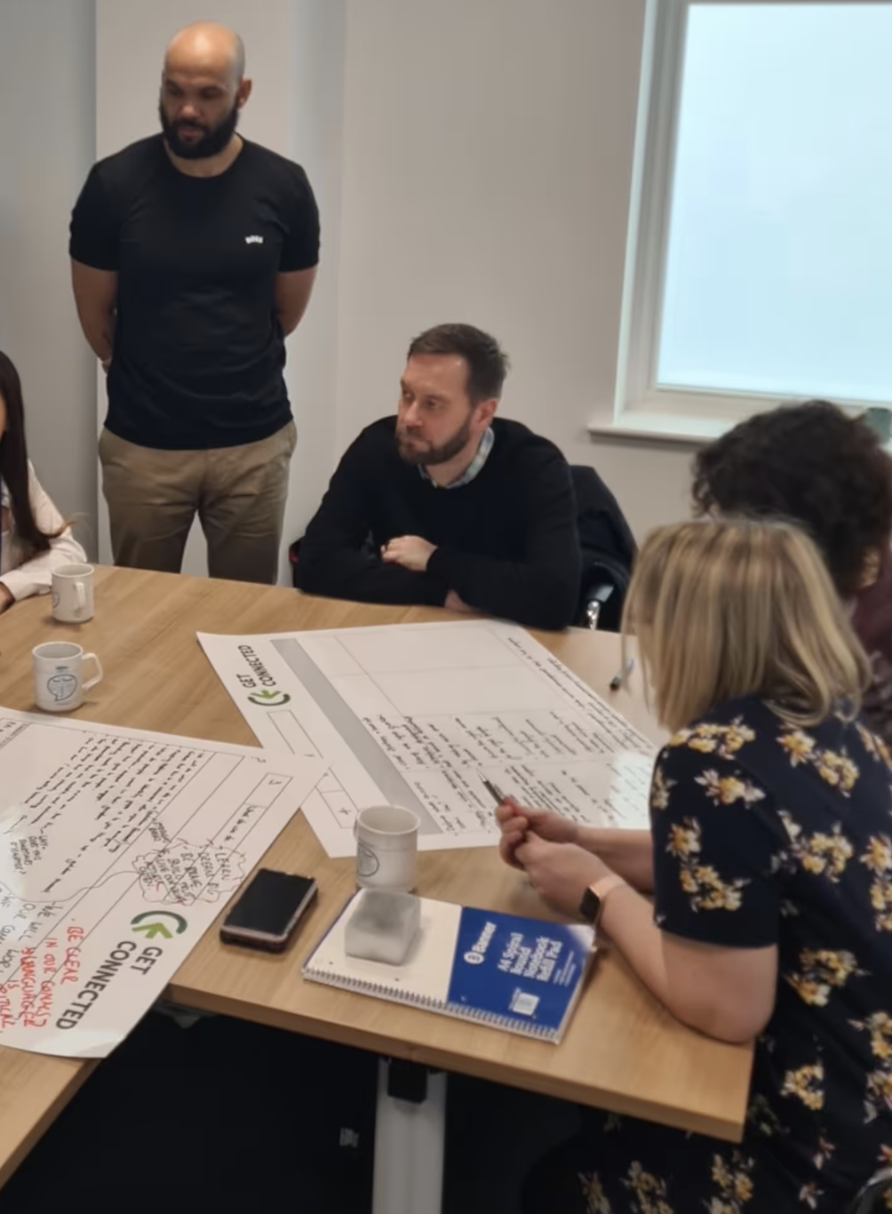 Group of participants collaborating around a table during a workshop session, discussing notes and project sheets.