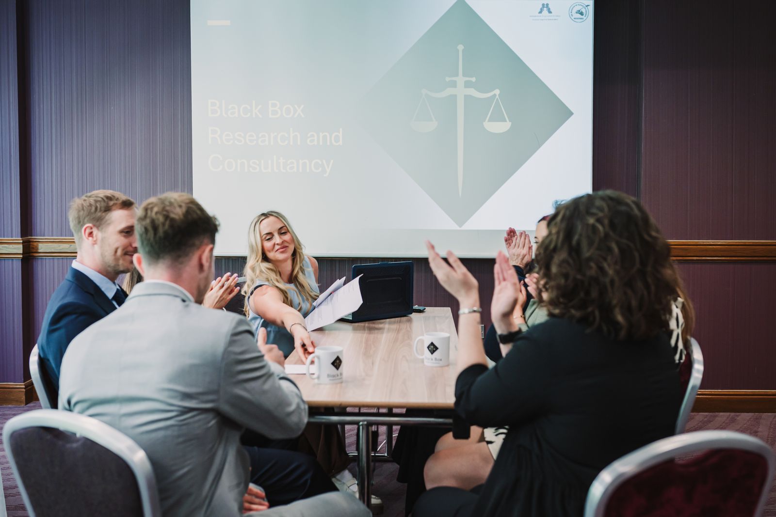 Group of participants engaged in a collaborative meeting with a presentation screen in the background.